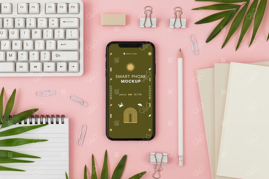 چیدمان تخت و نمای بالا از کیبورد سفید، موبایل و لوازم تحریر در پس‌زمینه صورتی با برگ‌های نخل؛ موکاپ فضای کار مینیمال و زیبا