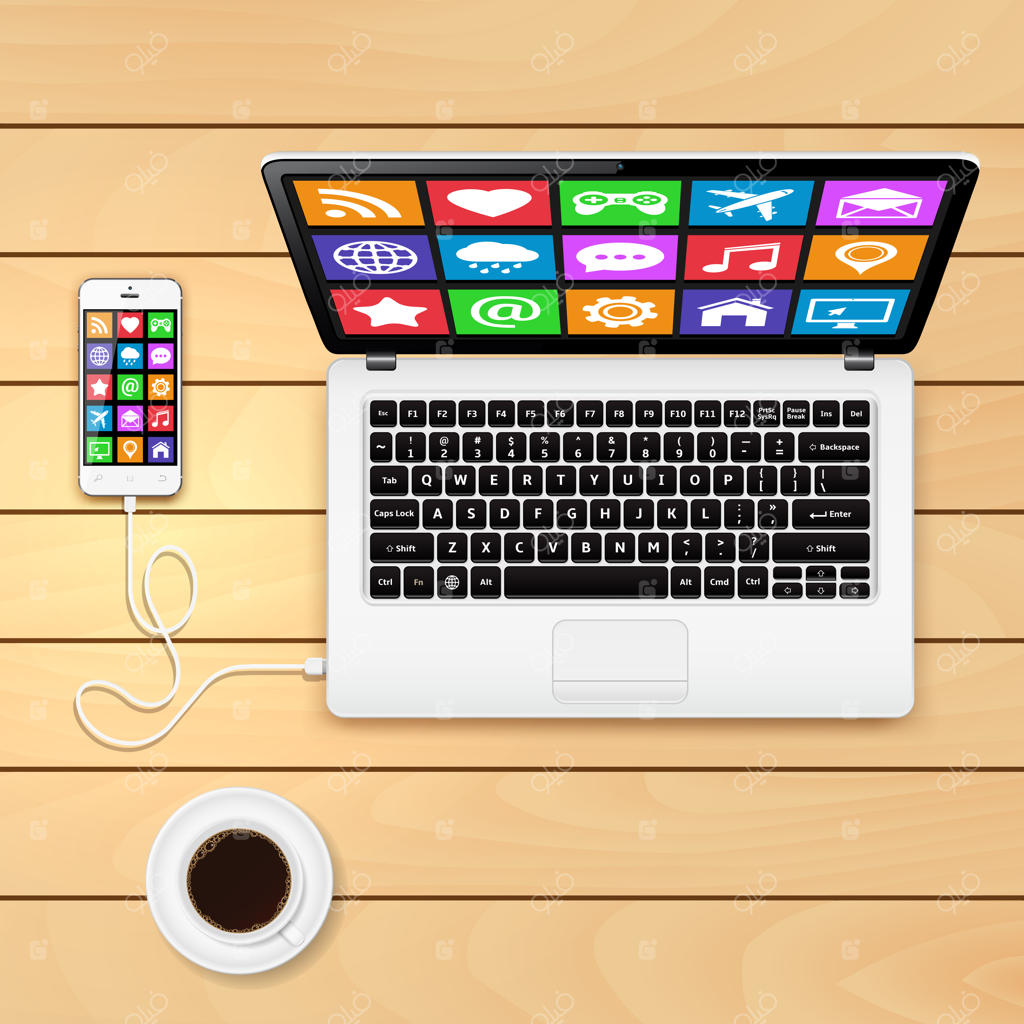 گوشی هوشمند متصل به لپ‌تاپ و فنجان قهوه روی میز